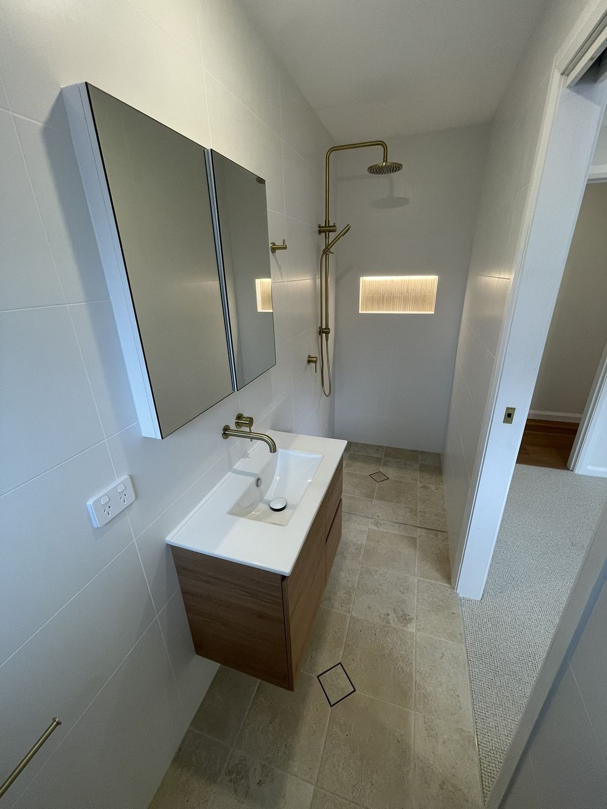 Small modern bathroom with a wall mirror, sink vanity, shower, and white tile floor.
