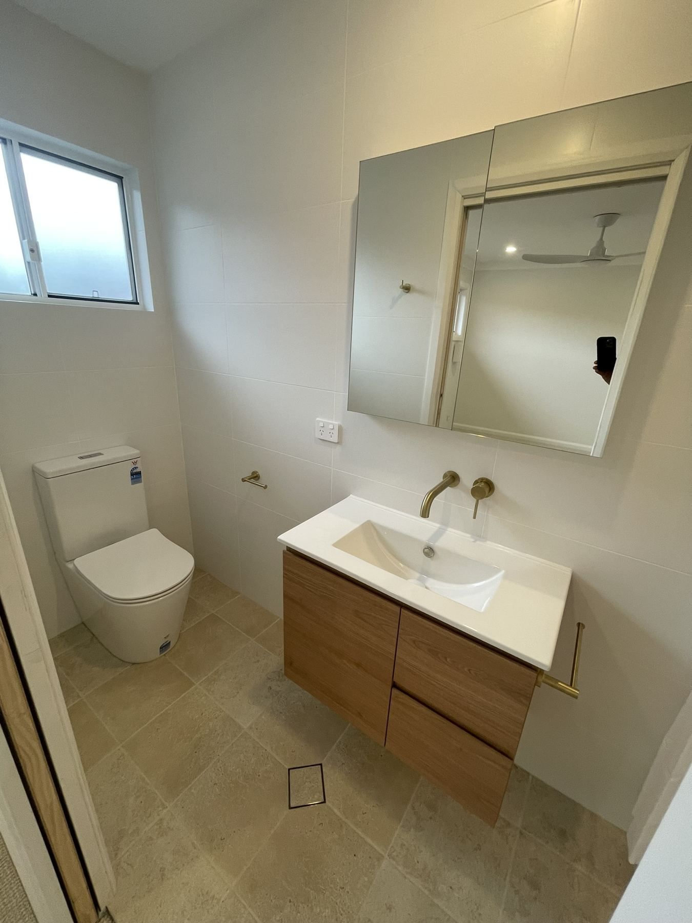 Small modern bathroom with toilet, vanity sink, mirror cabinet, and frosted window.