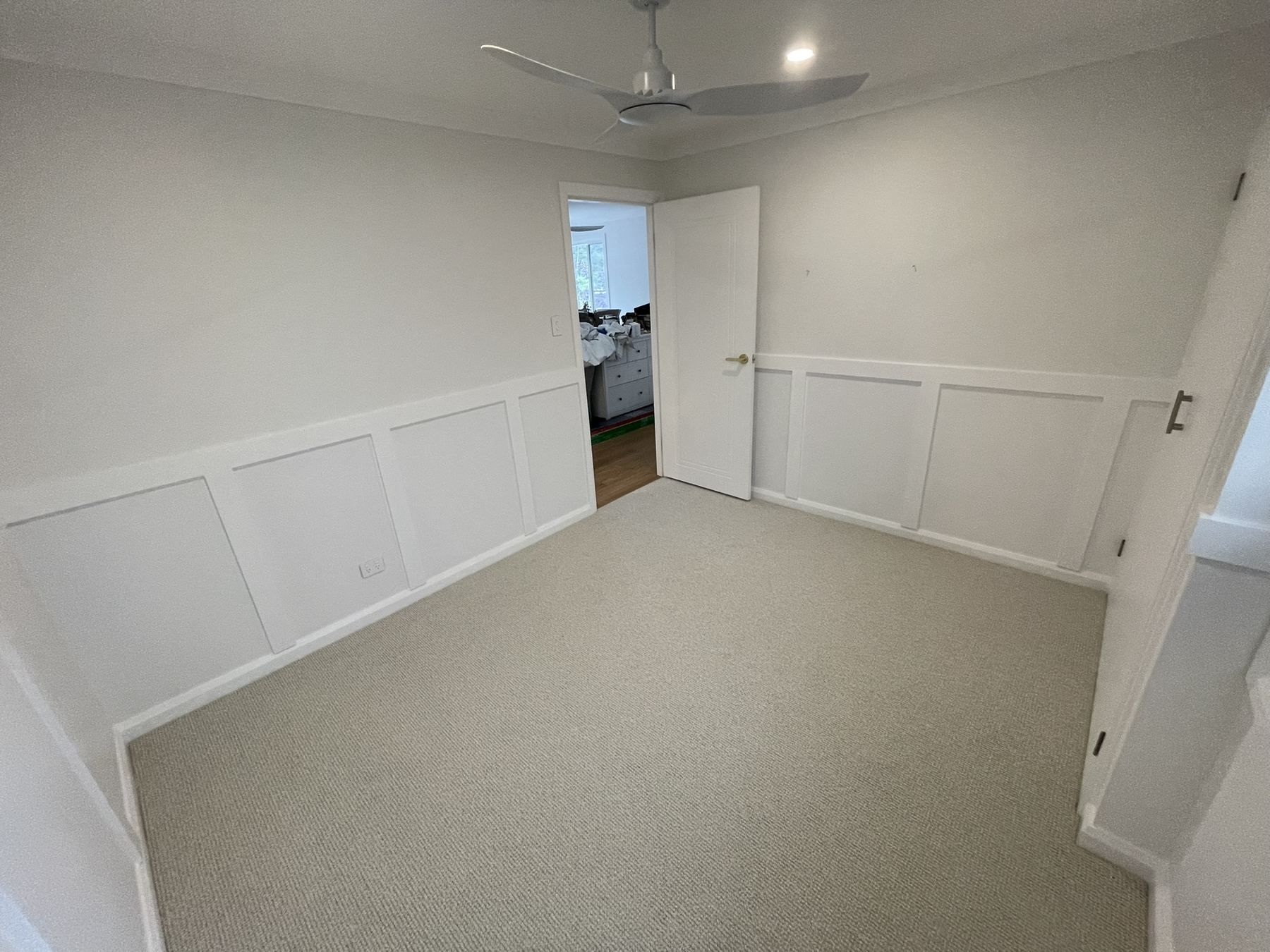 Empty white room with carpet, wainscoting, and an open doorway to another room.
