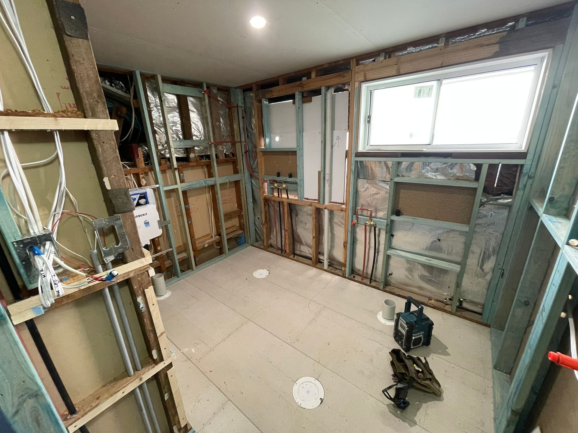 Unfinished bathroom under renovation with exposed studs, drywall, and tools on the floor