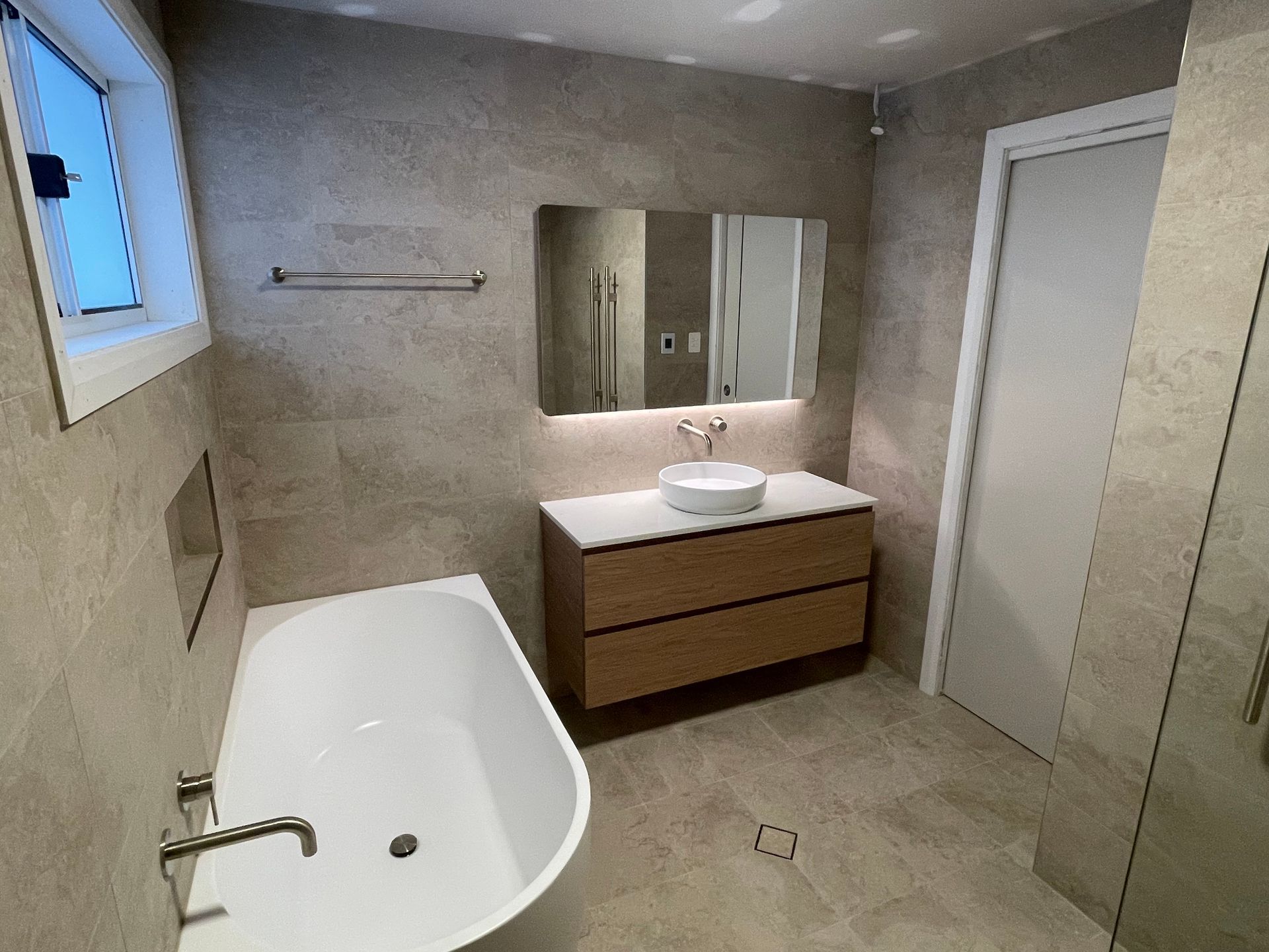 Modern bathroom with freestanding tub, double vanity, large mirror, and tiled walls