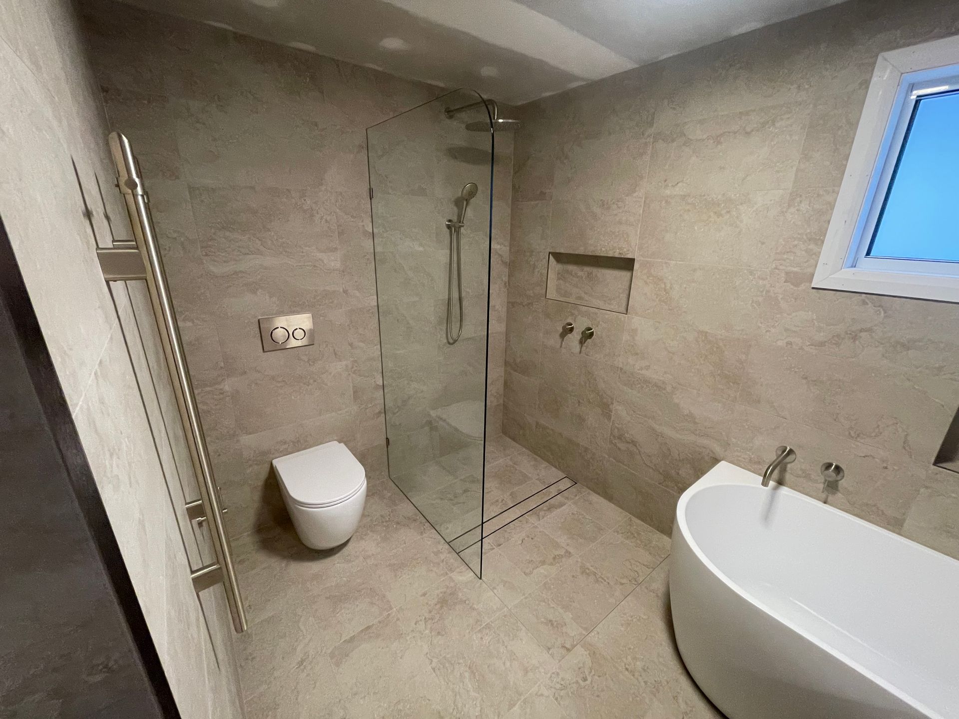 Modern bathroom with glass shower, wall-mounted toilet, and freestanding bathtub under a skylight