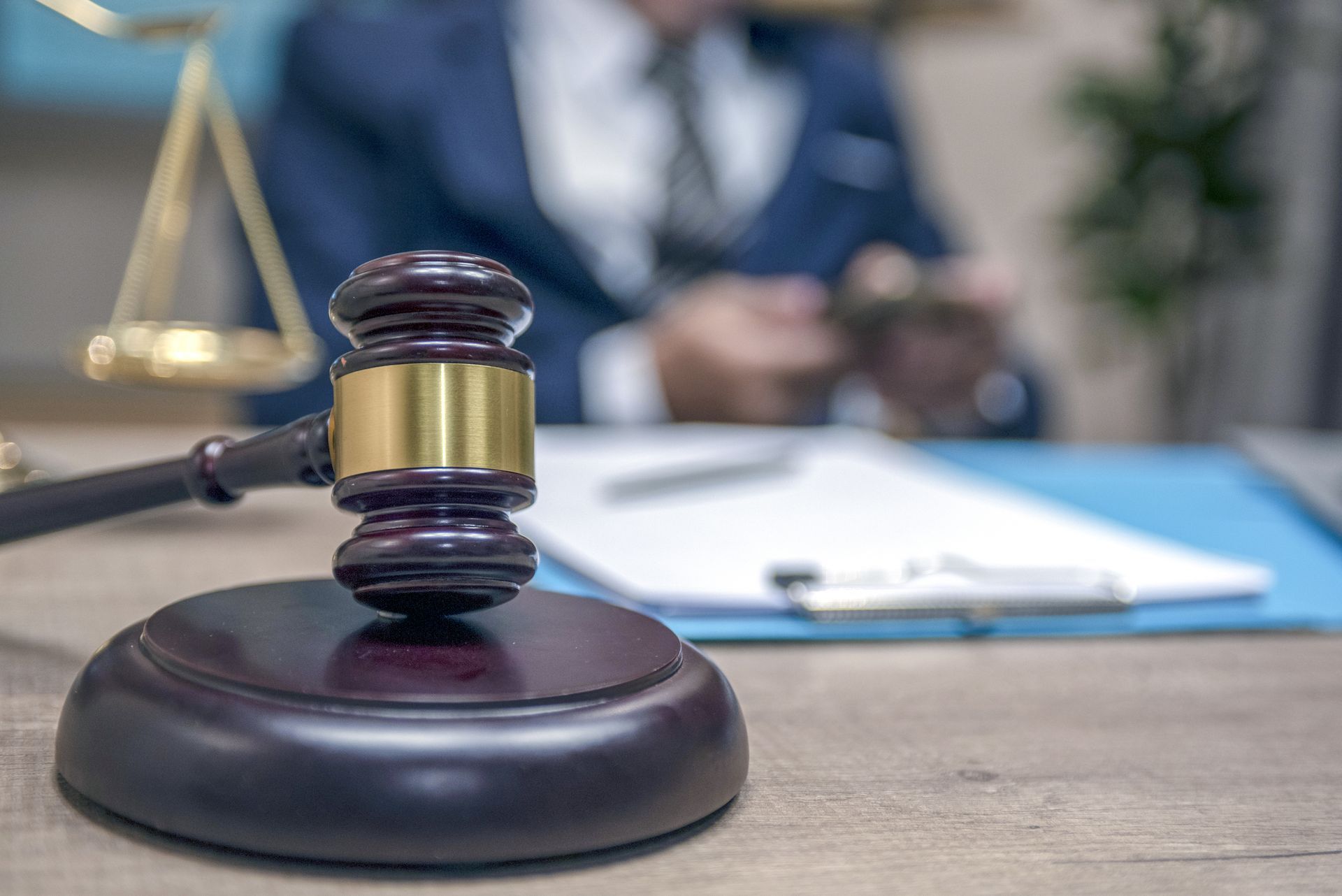 Gavel on wooden block in front of a lawyer in a blue suit, scales of justice in the background.