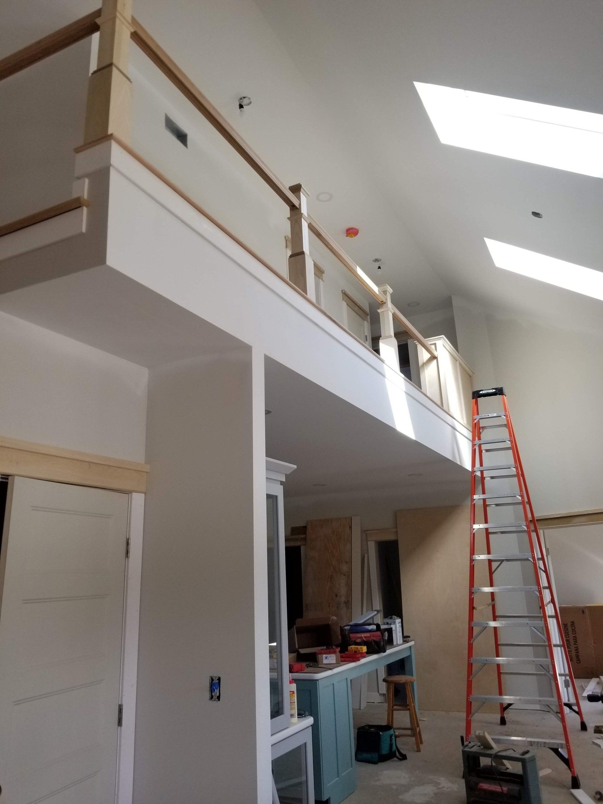 Interior view of a loft under construction with a tall ladder, white walls, and wooden railing.