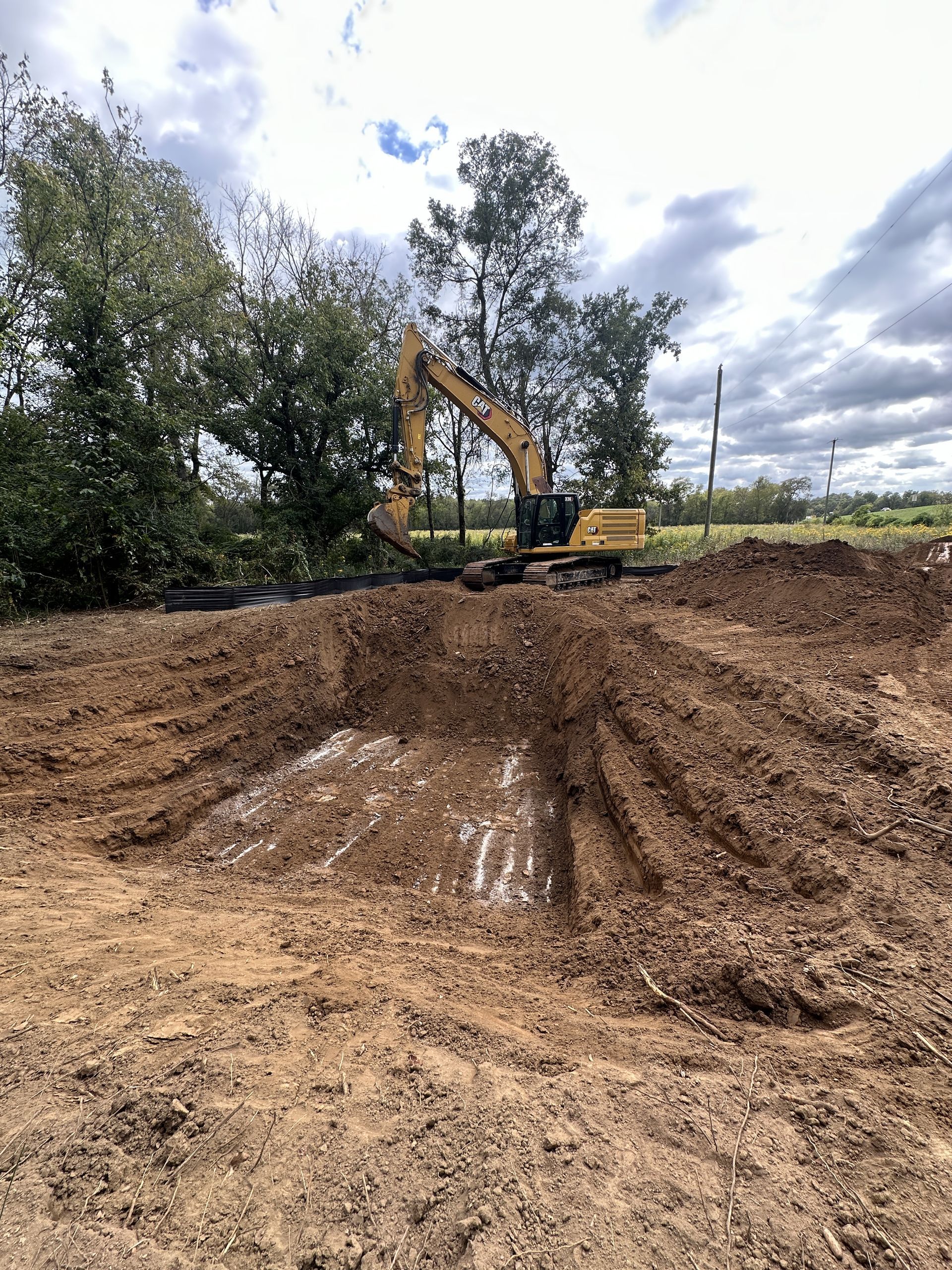 A large yellow excavator is digging a hole in the dirt in a field.