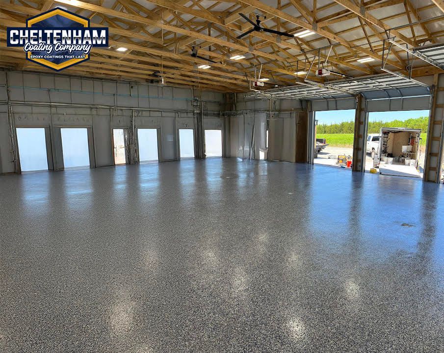 Large workshop with a polished gray speckled epoxy floor, wooden ceiling trusses, and open garage doors.