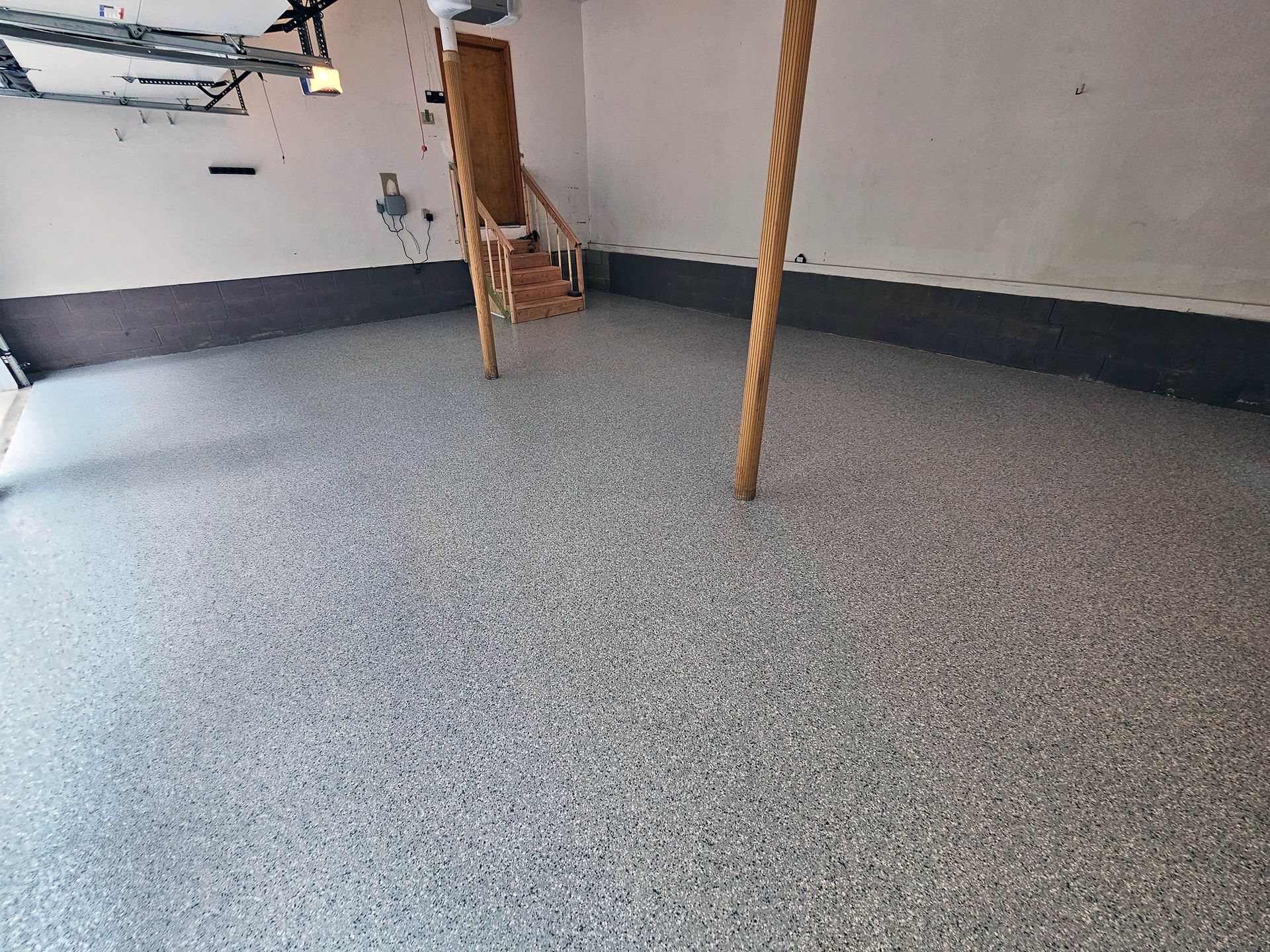 A garage interior with a grey, speckled epoxy floor and two wooden support posts.