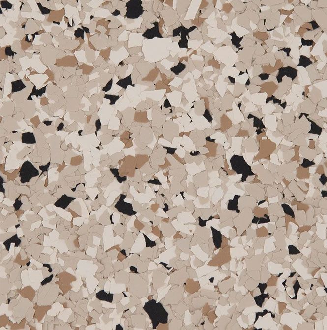 A close-up view of epoxy flooring flakes in a mix of cream, tan, and black colors, creating a speckled, textured pattern.