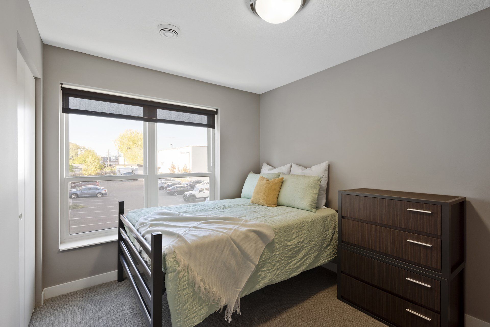 Apartment bedroom with large window, bed, and dresser