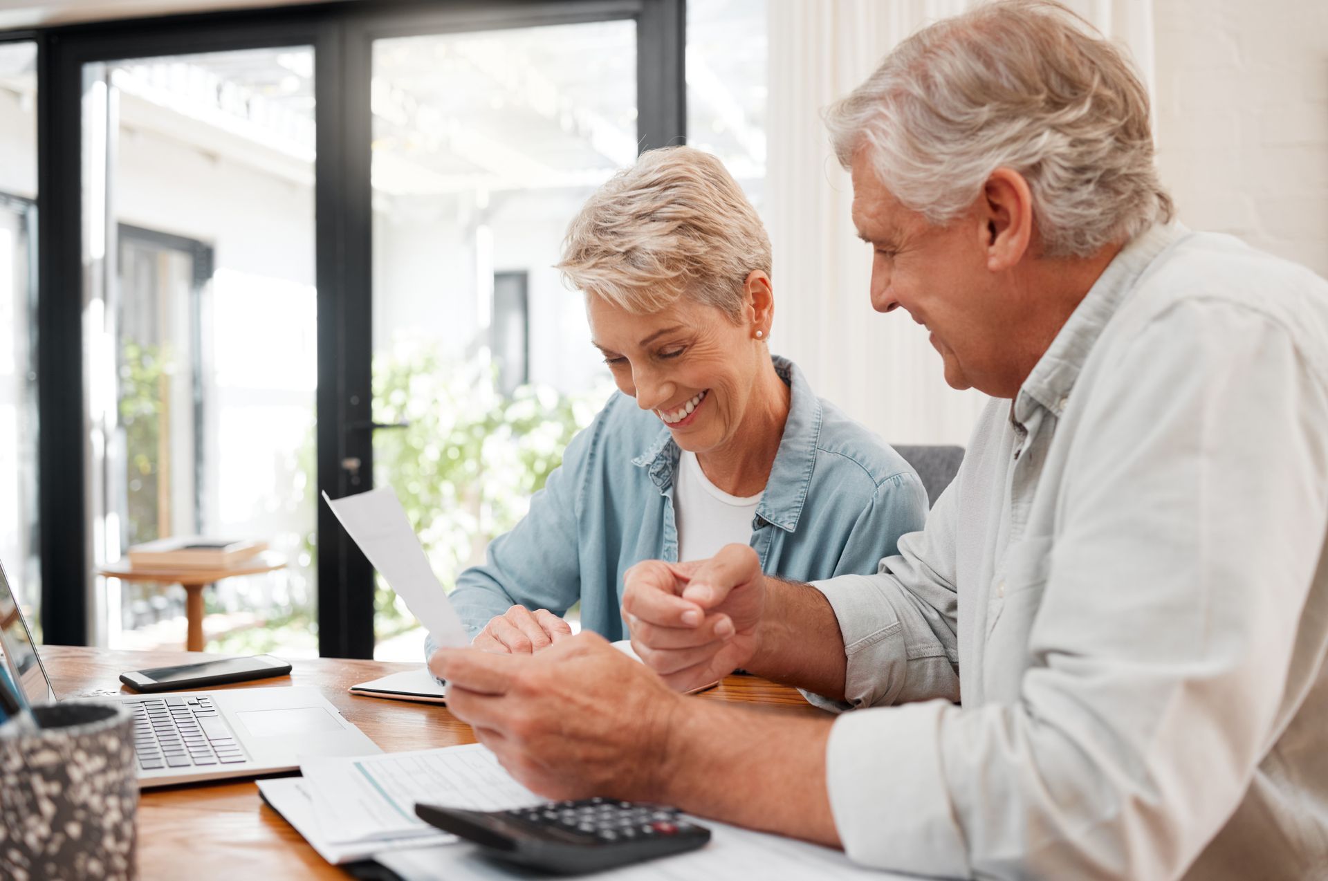Two people reviewing paperwork at a table with a calculator in a bright office