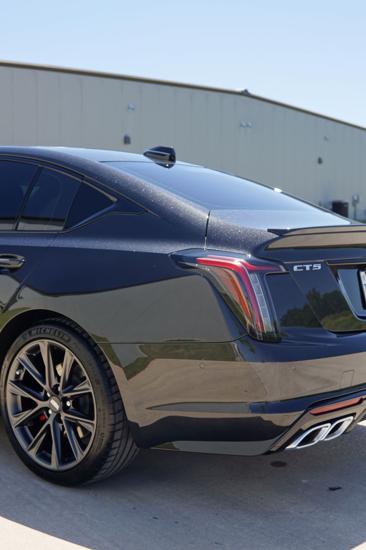 Black Cadillac CT5-V rear quarter view, parked on a sunny day, with dark rims and red taillights.