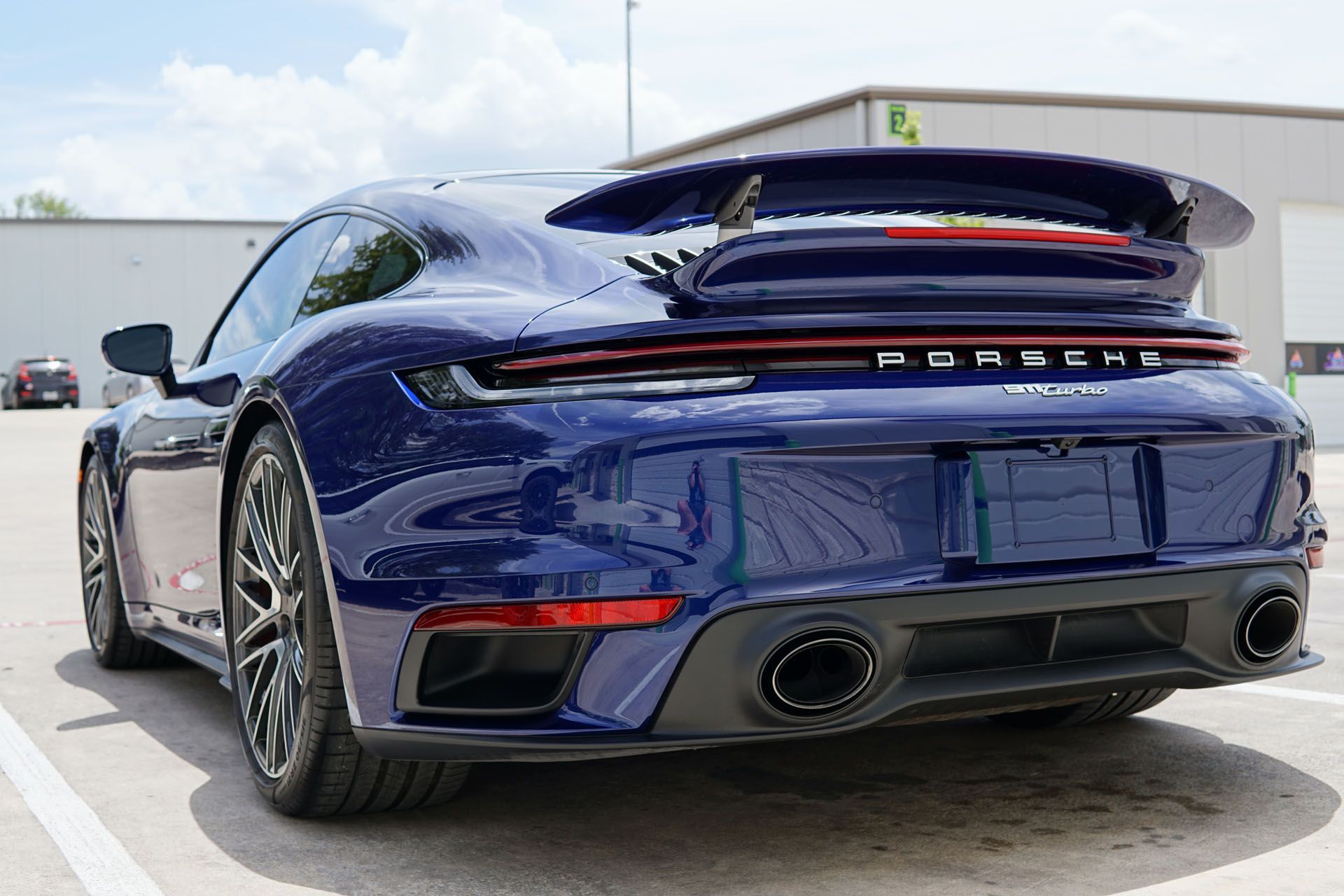 Dark blue Porsche 911 GTS coupe with spoiler, parked in front of a building.