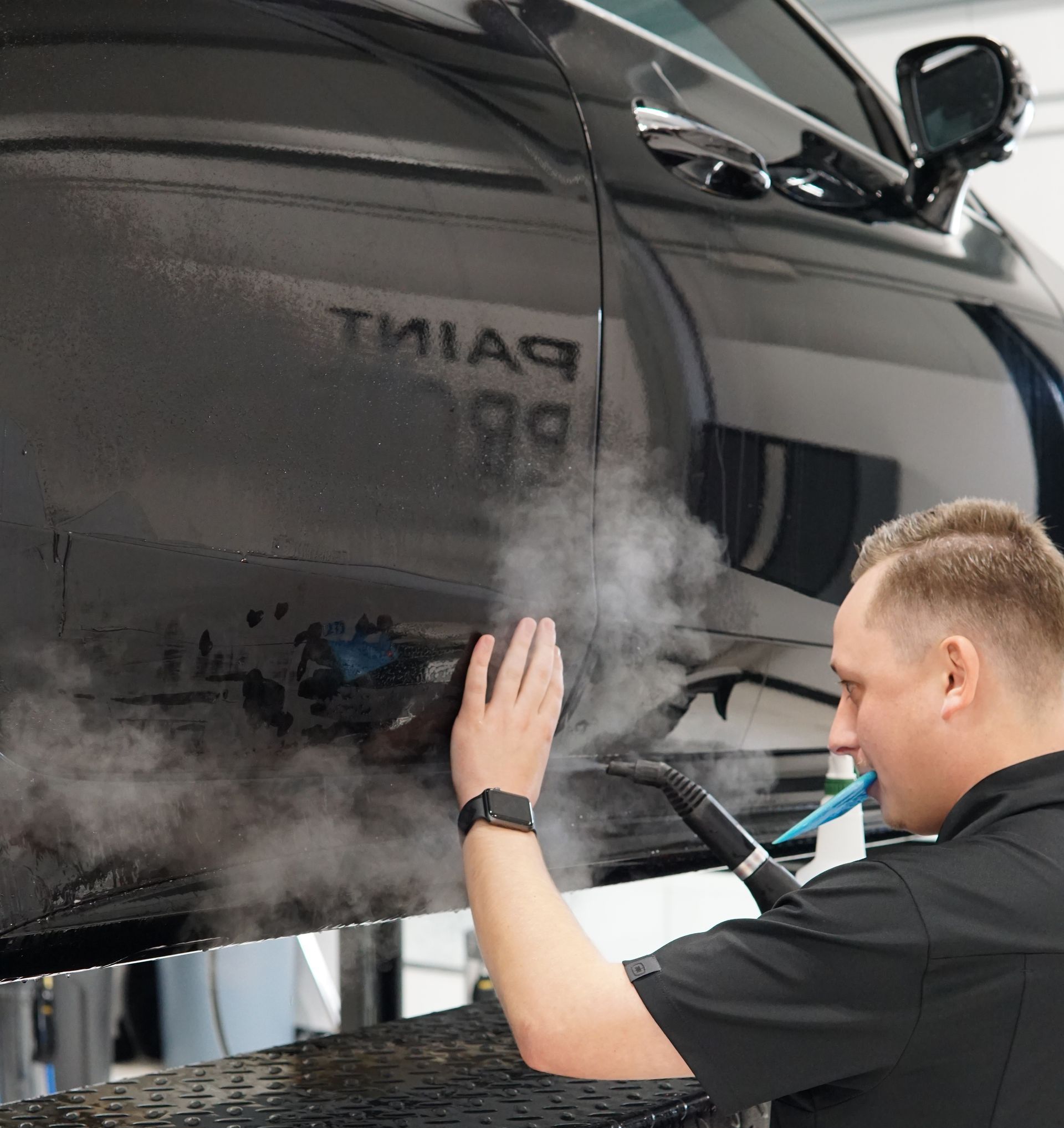 Person applying film to a black car fender, using a blue squeegee.
