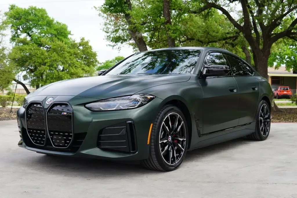 A green bmw 4 series is parked in a driveway next to trees.