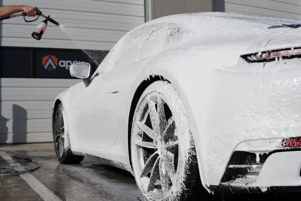A person is washing a white sports car with foam.