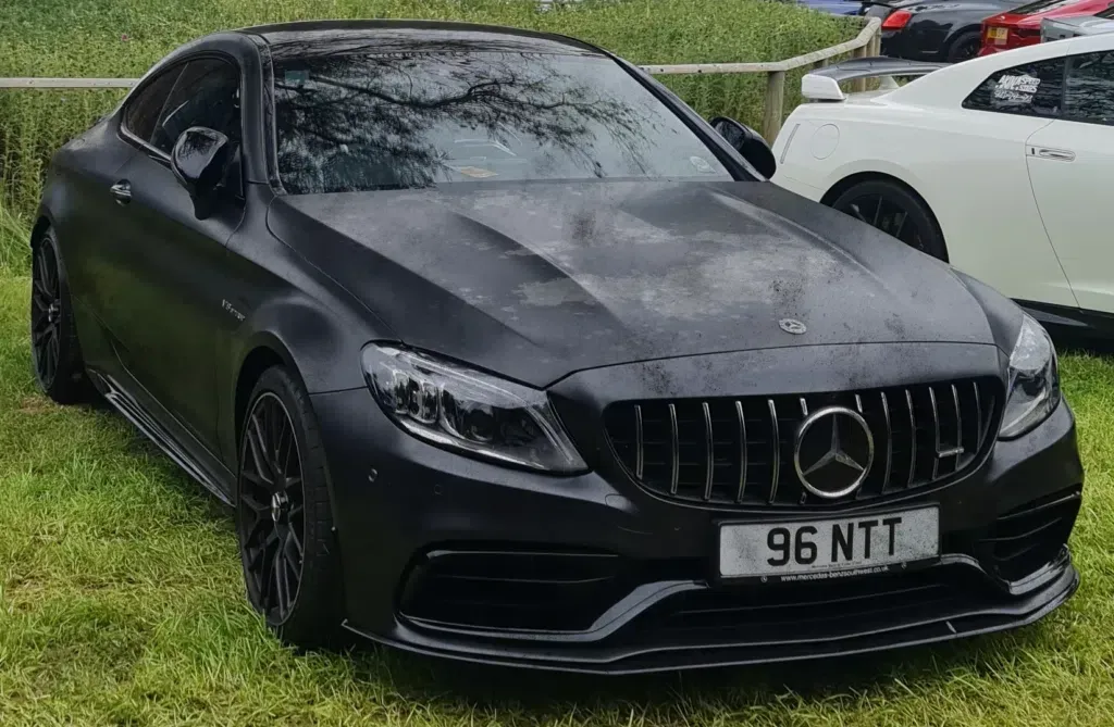 A black mercedes benz c63 amg coupe is parked in the grass.