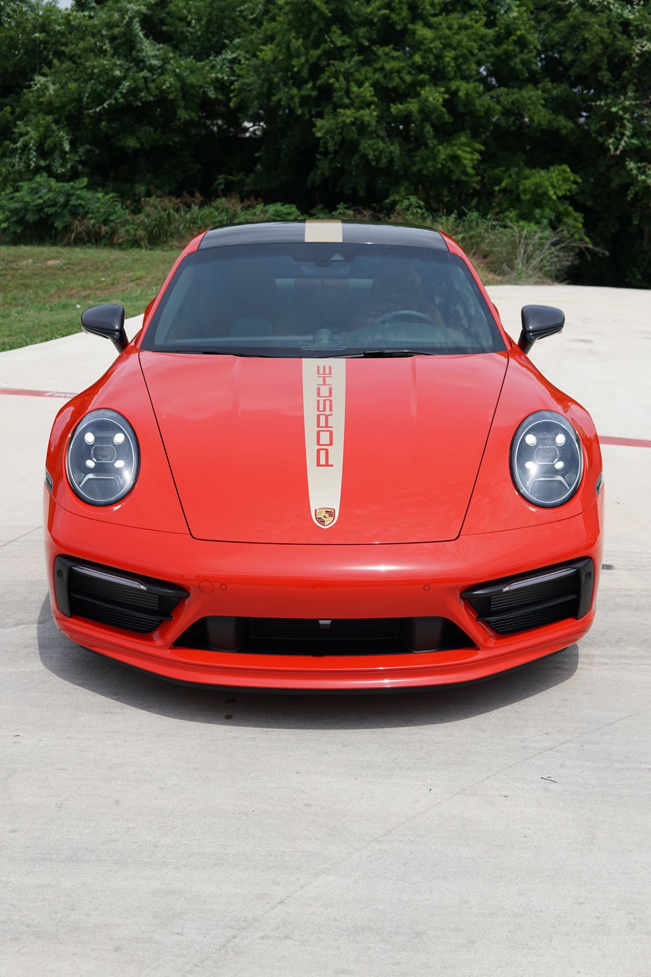 Red Porsche sports car with gold racing stripe on a paved area.