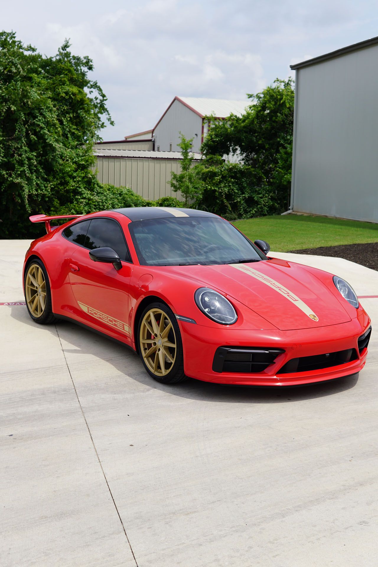 Red Porsche 911 with gold accents parked outside on concrete.