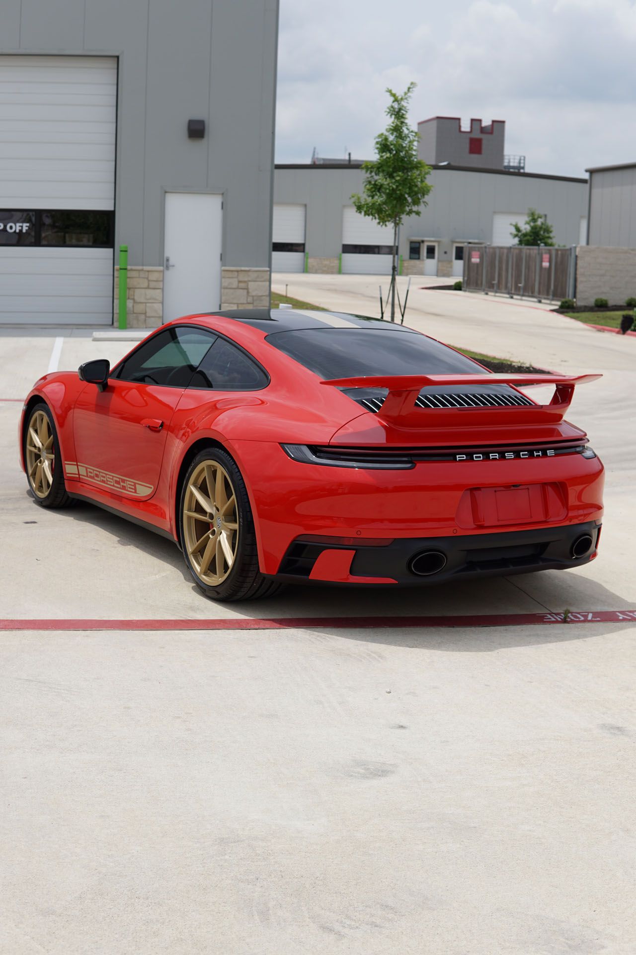 Red Porsche 911 parked outdoors, black roof, gold wheels, rear view.