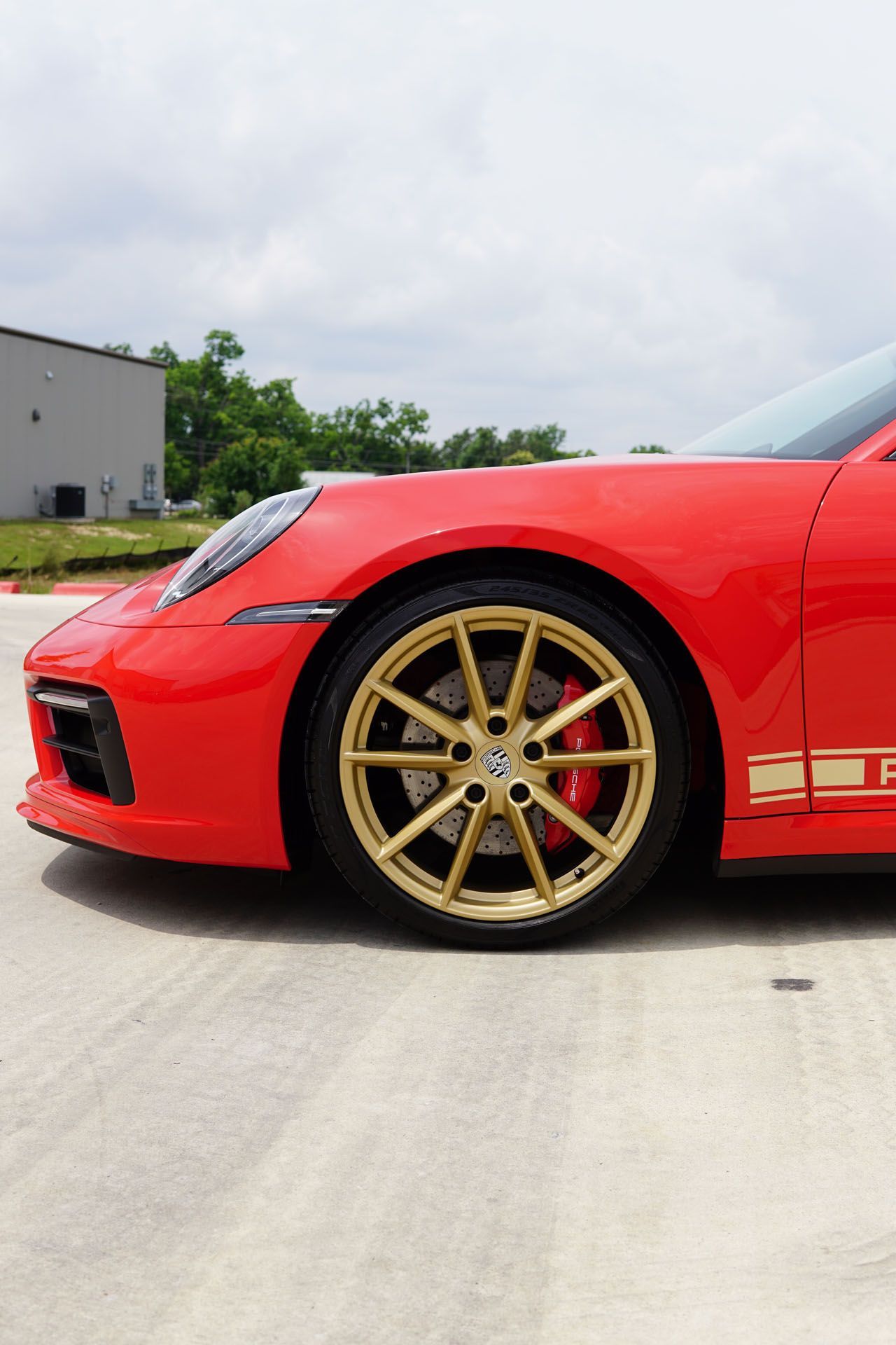 Red Porsche sports car with gold rims and red brake calipers, parked on a paved surface.