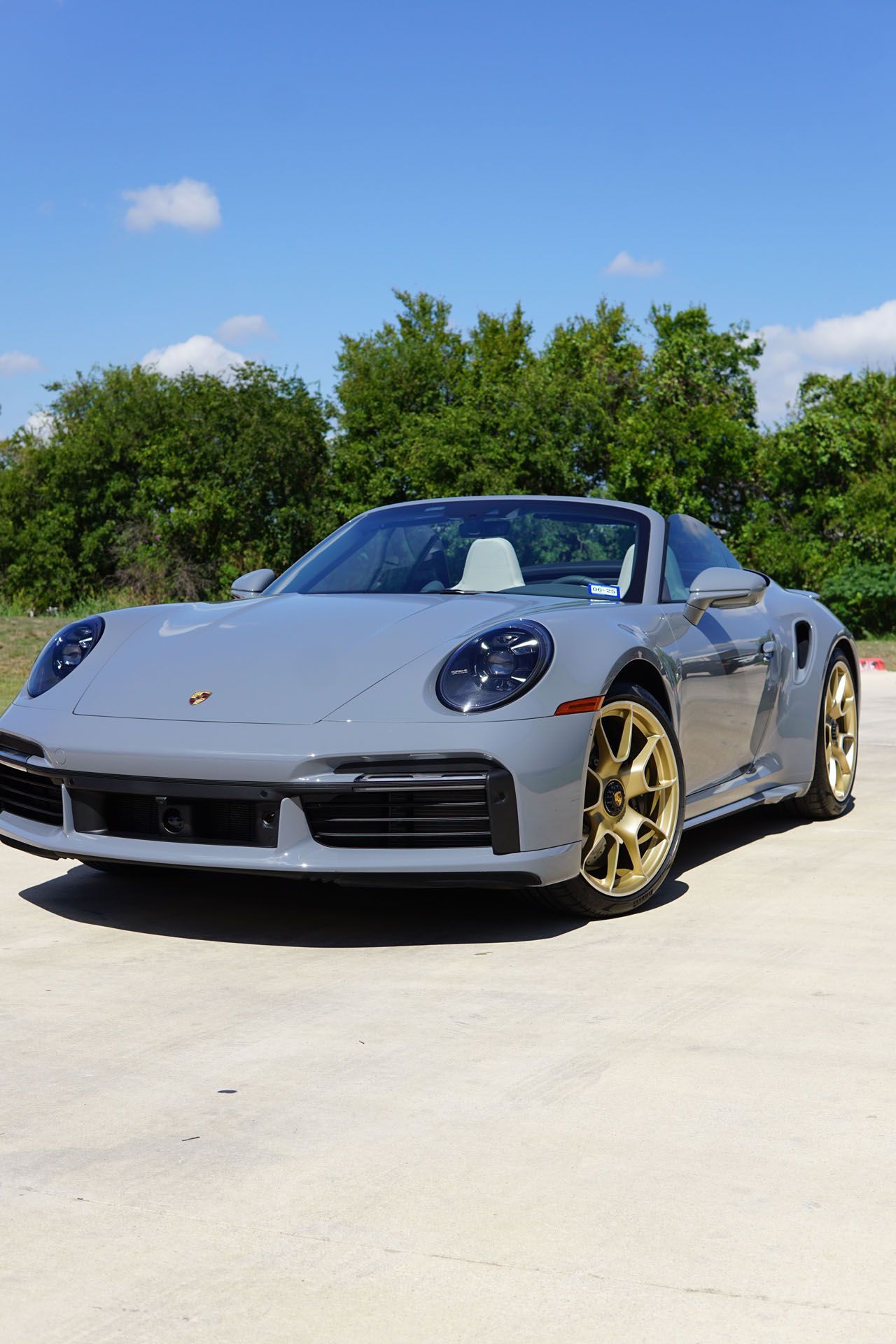 Gray Porsche convertible with gold wheels parked outside on a sunny day.