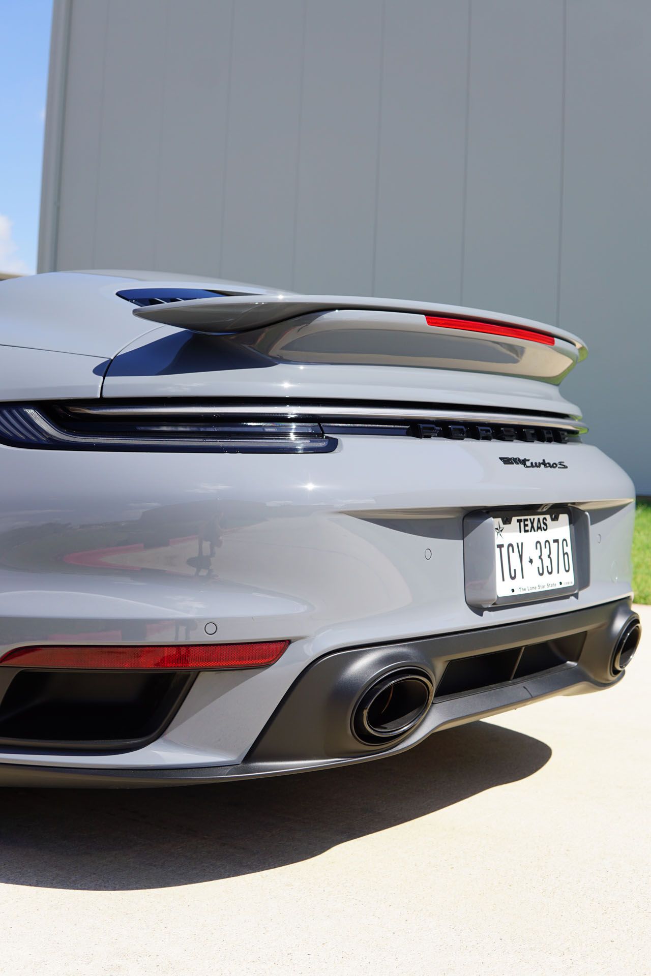 Gray Porsche 911 rear view with spoiler, Texas license plate, and black exhaust.