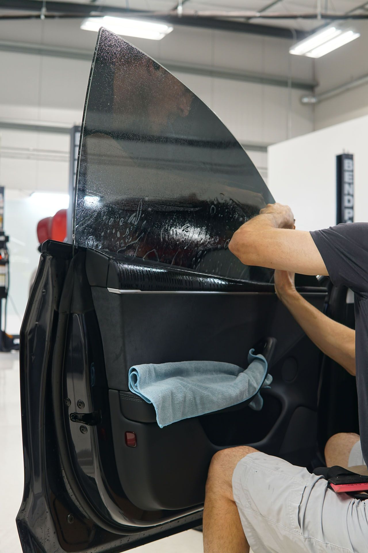 Person applying tinted film to a car window in a shop, using a cloth.