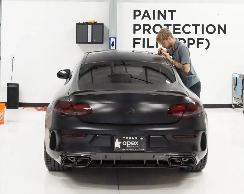 A man is wrapping a black car with paint protection film.
