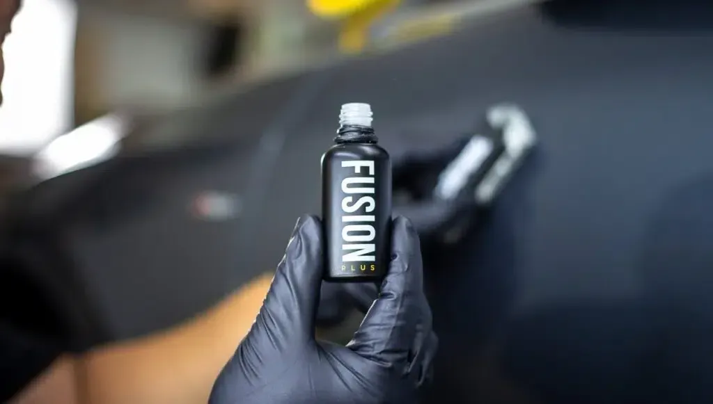 Person applying car ceramic coating, holding a black bottle labeled 