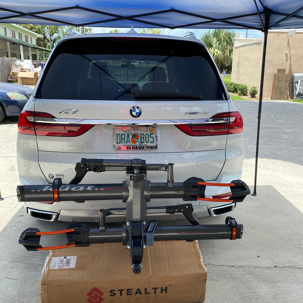 White BMW SUV with a bike rack mounted on a cardboard box under a blue canopy.