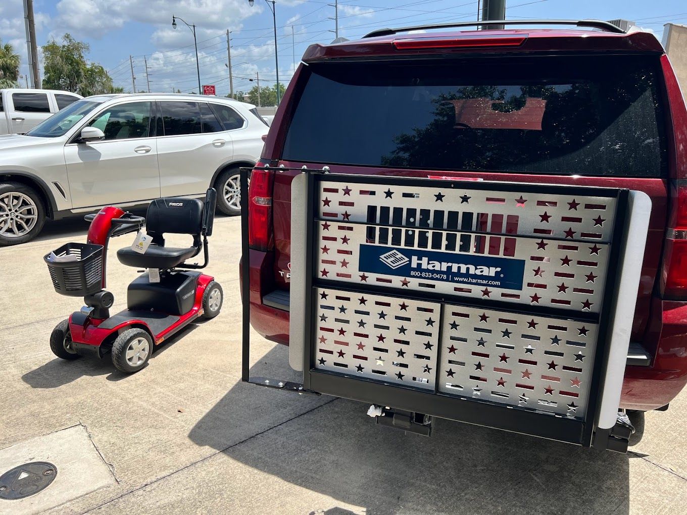 Red SUV with a rear-mounted cargo carrier at a parking lot, next to a red mobility scooter.