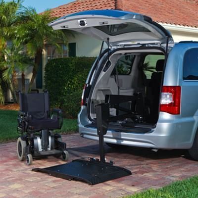 Wheelchair lift deployed beside a silver minivan in a driveway, with the rear hatch open.