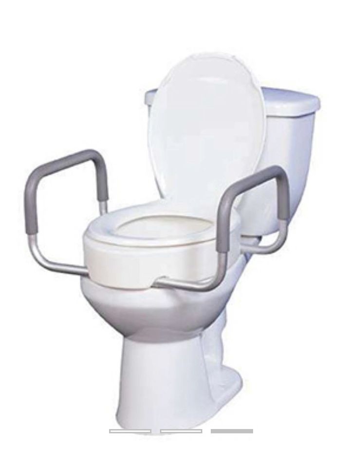 White toilet with raised seat and gray armrests for accessibility support