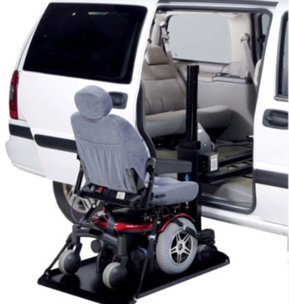 Wheelchair lift beside open van door, with a wheelchair secured on the platform.