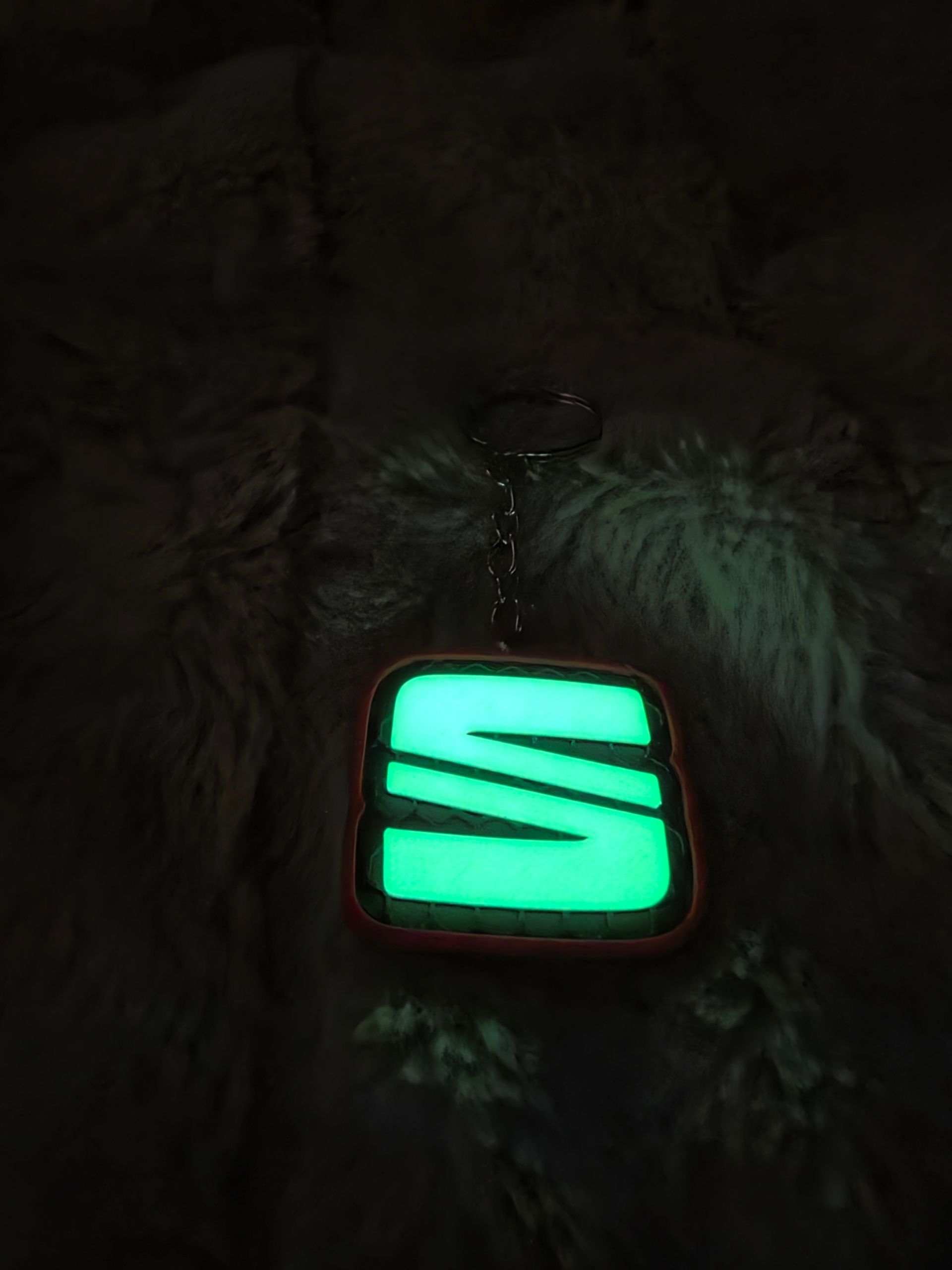Neongroene, oplichtende SEAT-logohanger op een donkere, bedrukte stoffen achtergrond.