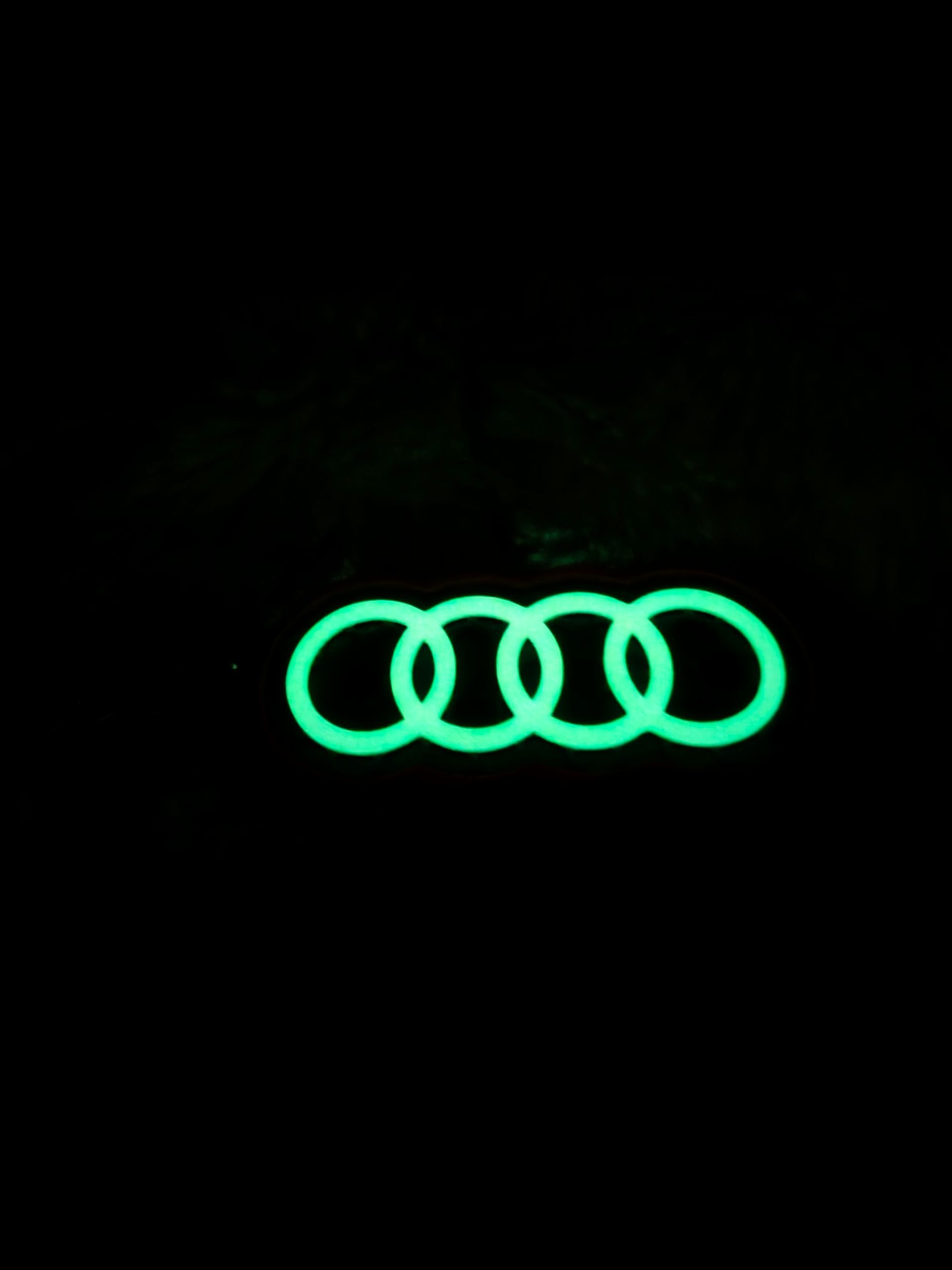 Lichtgevend groen Audi-logo met vier ringen op een zwarte achtergrond