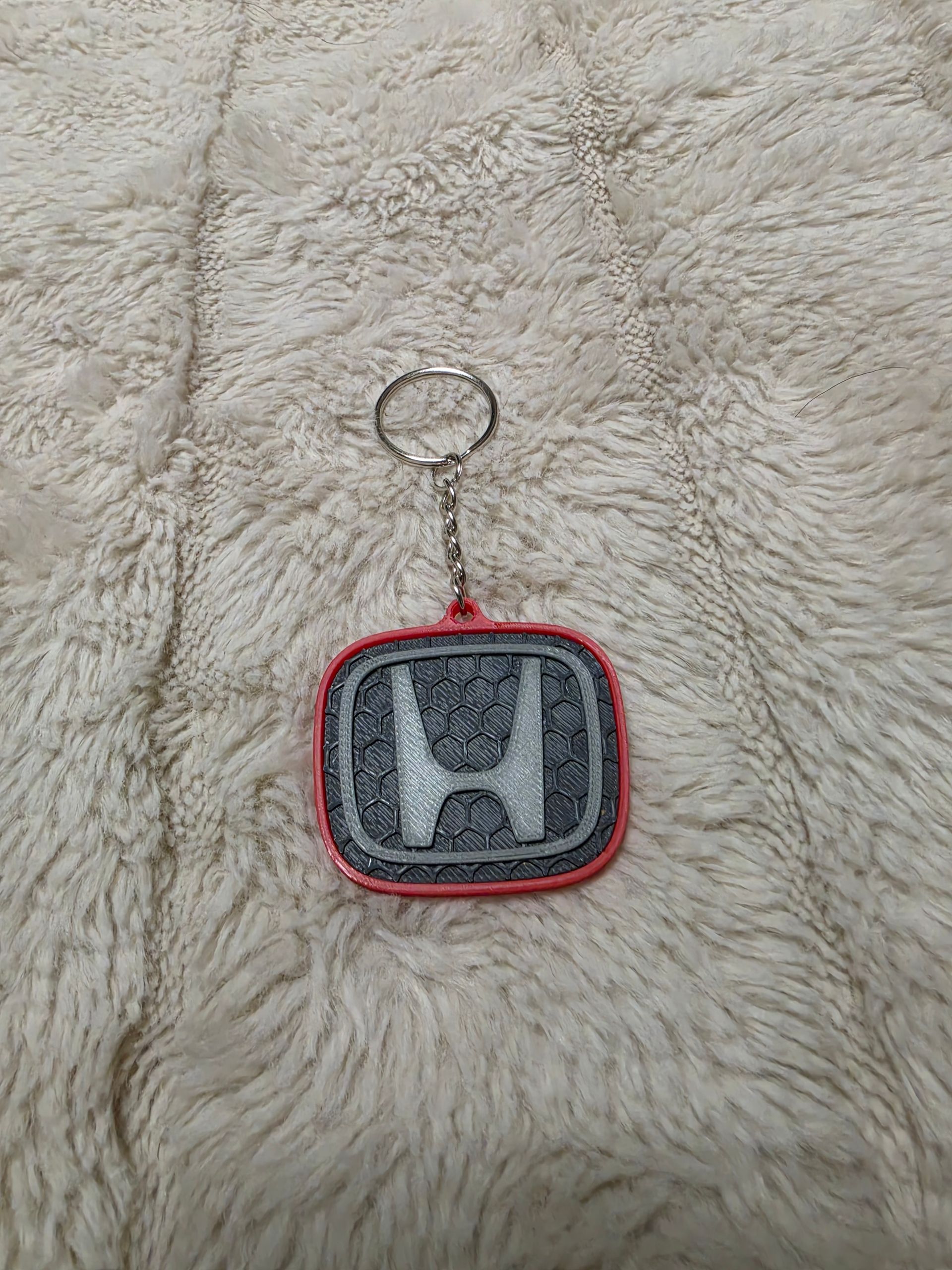 Sleutelhanger met Honda-logo en turquoise neon omlijning op een donkere stoffen achtergrond.