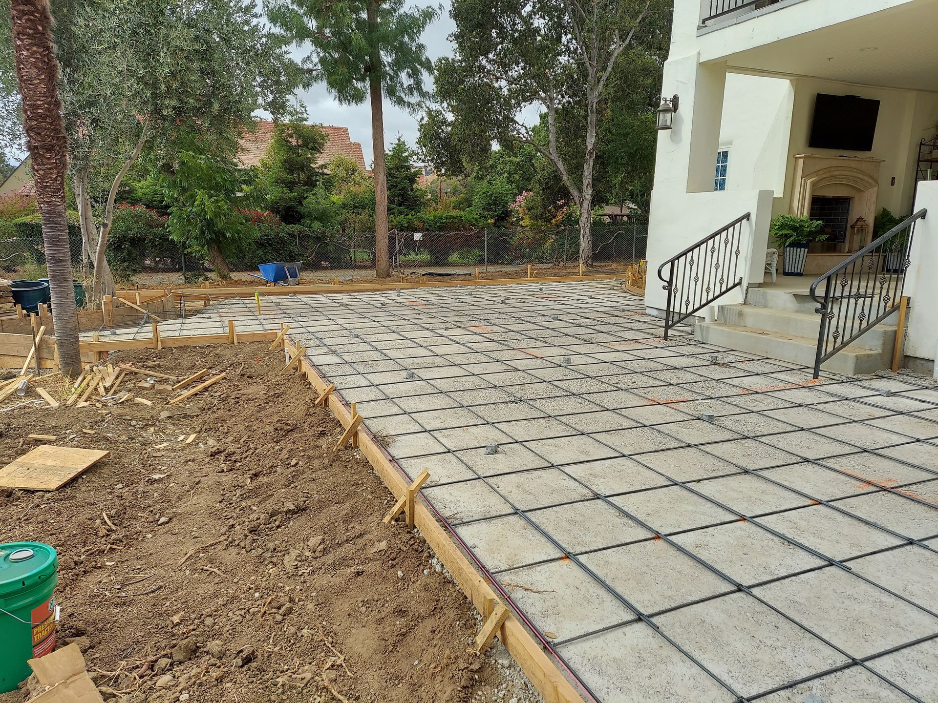 A patio under construction with square stone pavers and black grid dividers, framed by wooden forms next to a house.