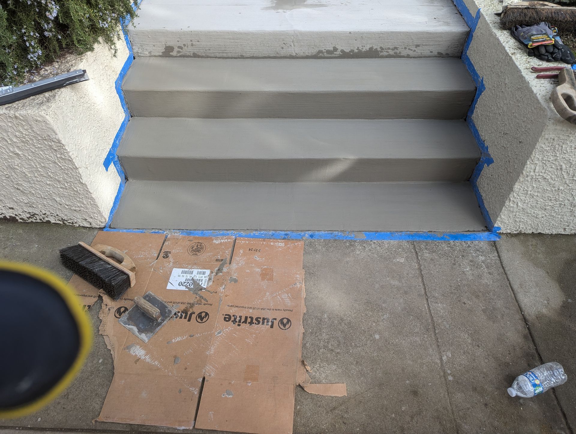 Freshly poured concrete stairs with blue masking tape along the edges, next to a cardboard sheet and masonry tools.