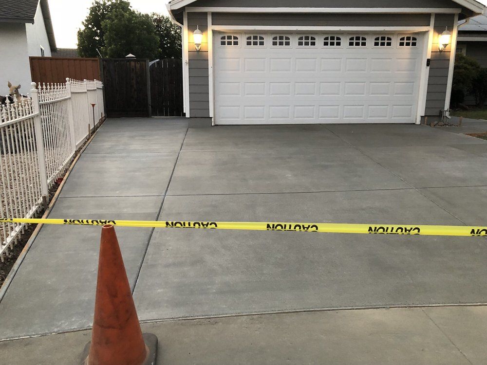 New concrete driveway blocked by caution tape and traffic cone. Garage in background.