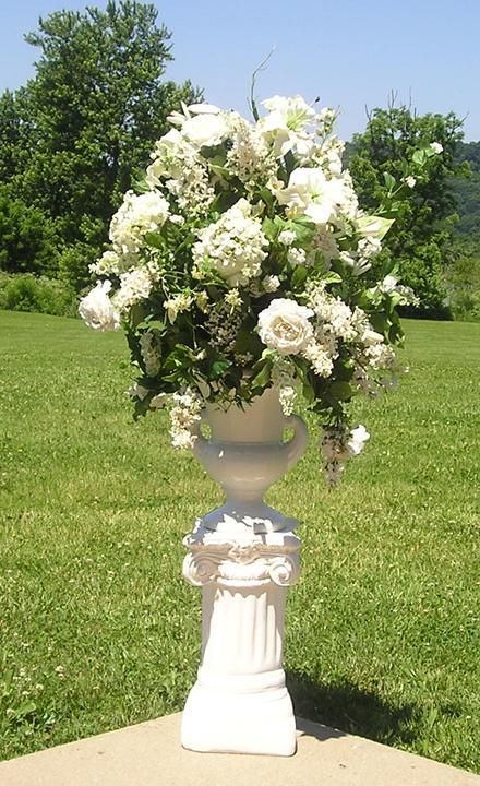 A white vase filled with white flowers is sitting on top of a concrete pedestal.