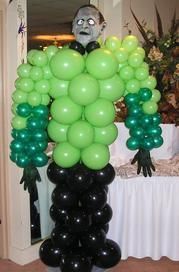 A monster made out of green and black balloons is standing in front of a table.