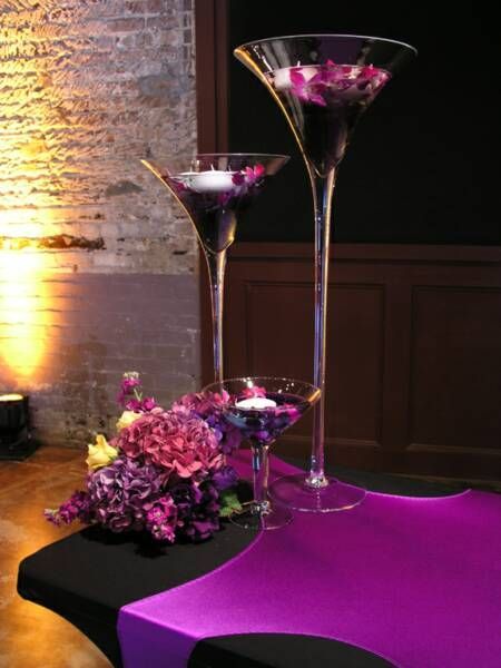 Two martini glasses with purple flowers and candles in them