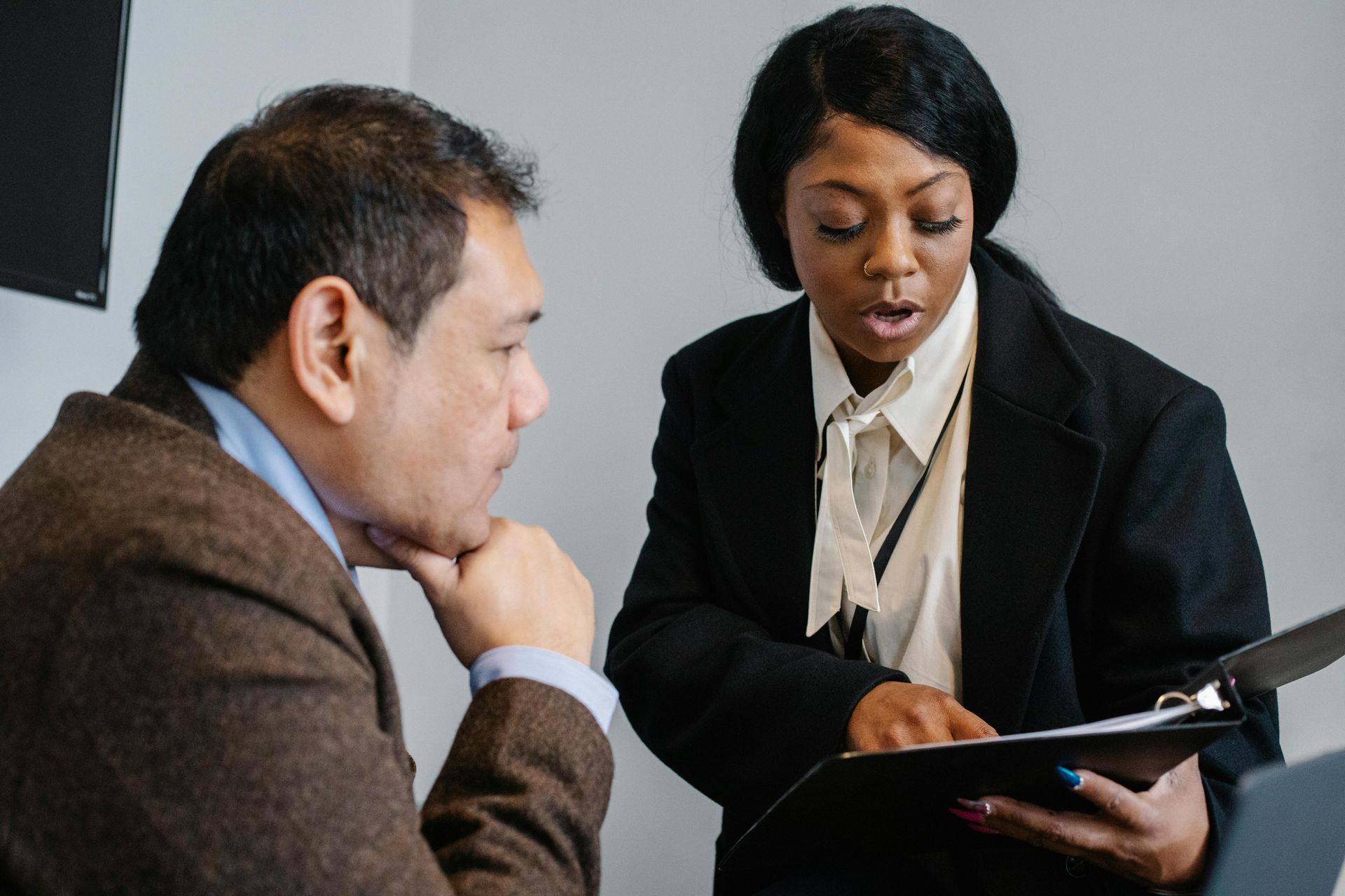 Man and woman in business attire reviewing documents; man listens while woman points.