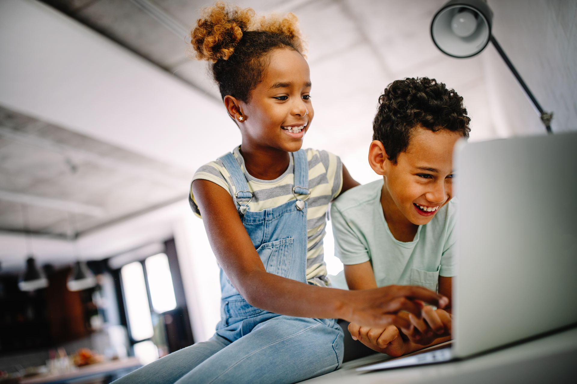 A boy and a girl are sitting on a table looking at a laptop computer.