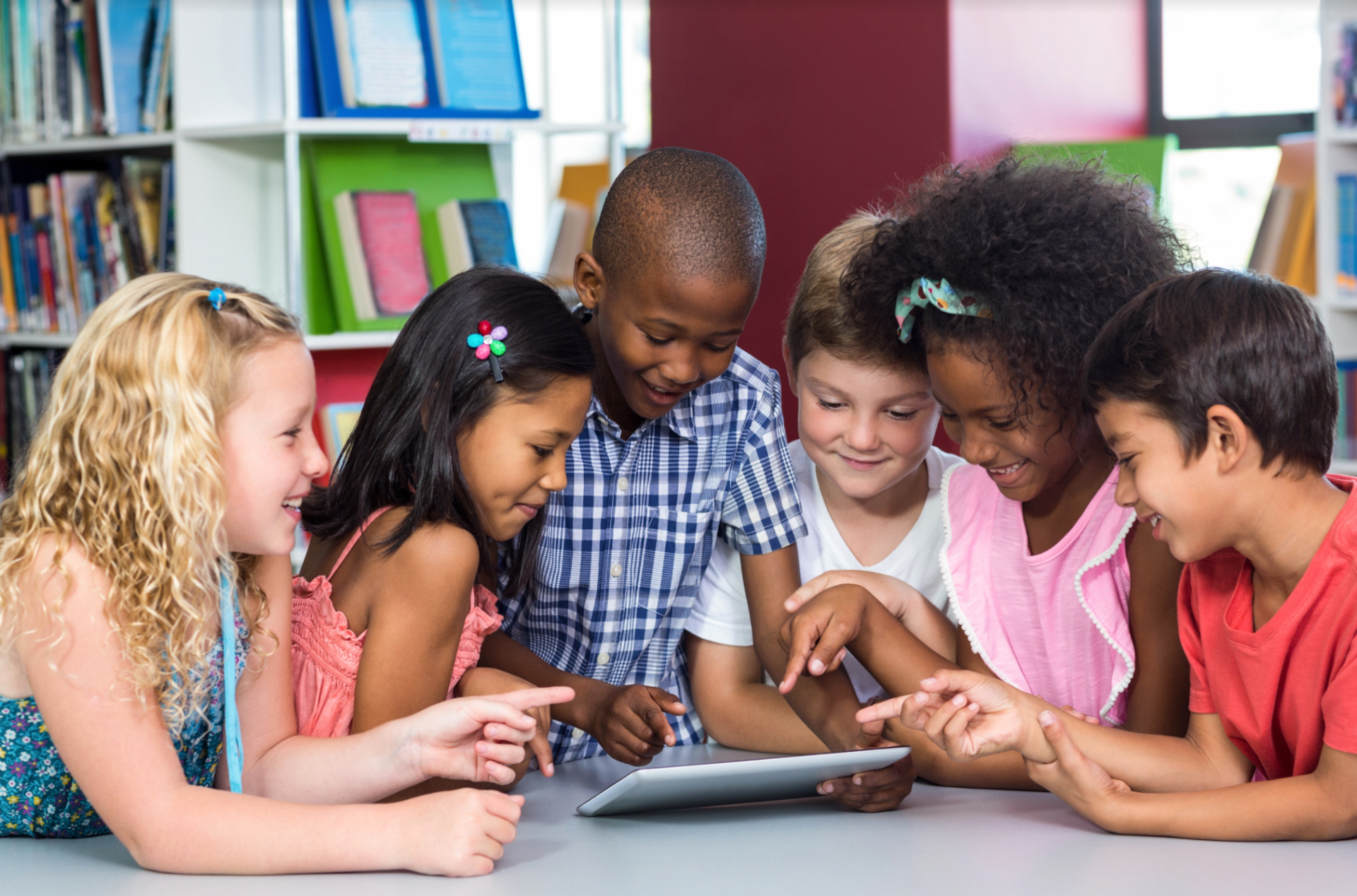 A group of children are sitting around a table looking at a tablet computer.
