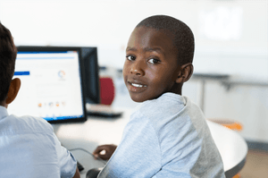 A young boy is sitting at a desk in front of a computer.