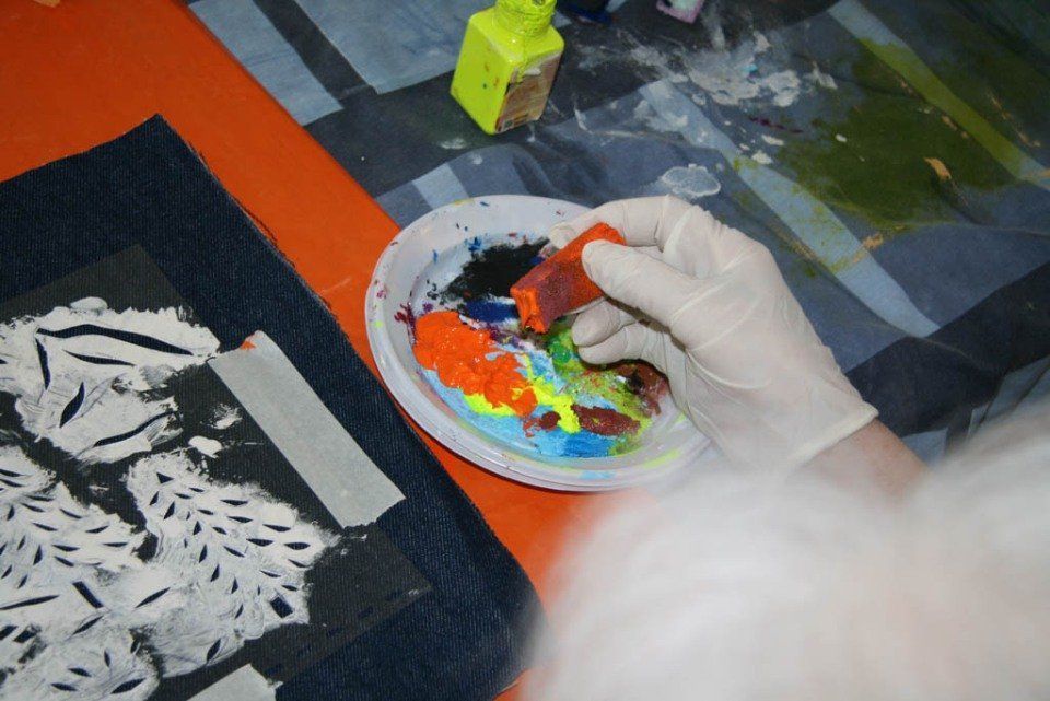 Una mano guantata mescola colori vivaci su una tavolozza accanto a un'opera d'arte in bianco e nero su un tavolo da lavoro.