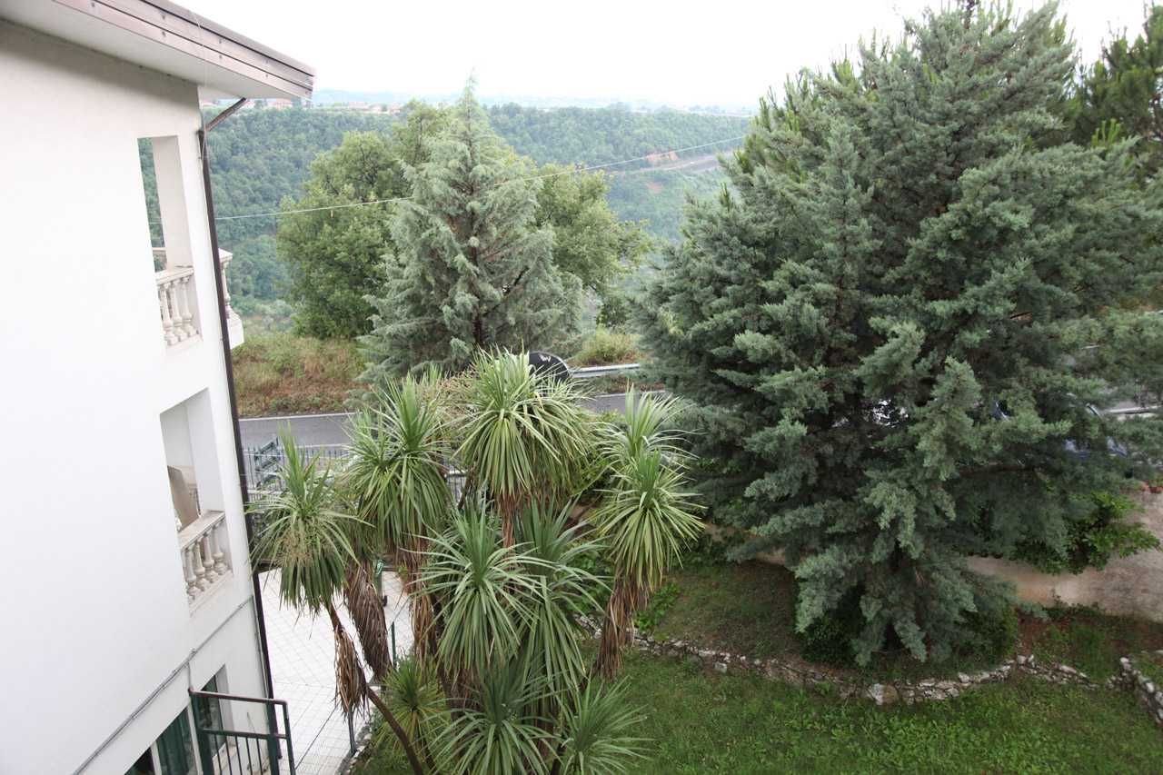 Un edificio bianco accanto a un rigoglioso giardino con alberi e, in lontananza, una verde collina.