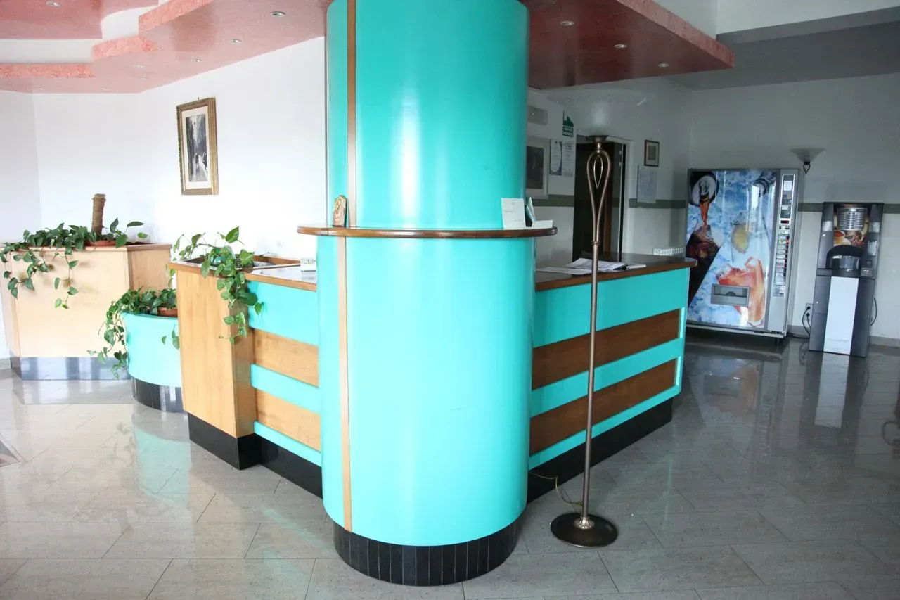 Atrio vuoto dell'hotel con reception turchese e piante in vaso su un pavimento lucido.